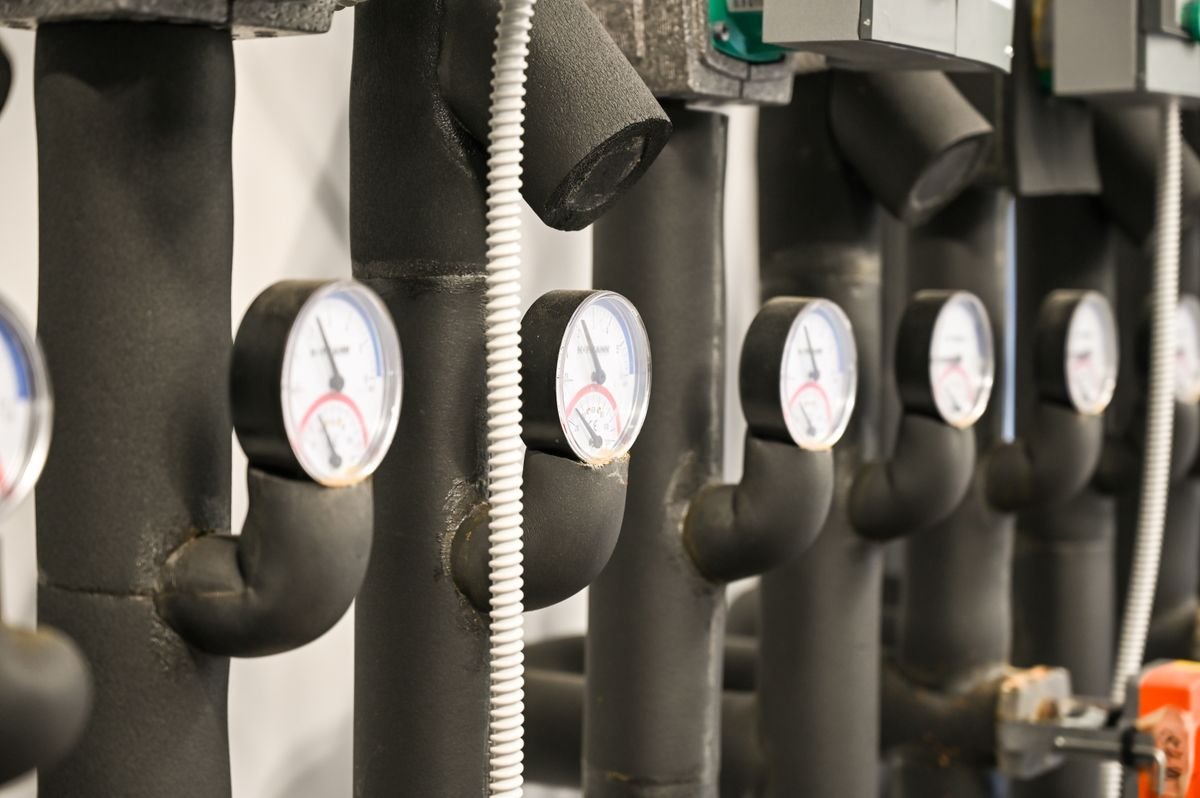 Plumber checking pipework and isolation valves in a commercial building plant room